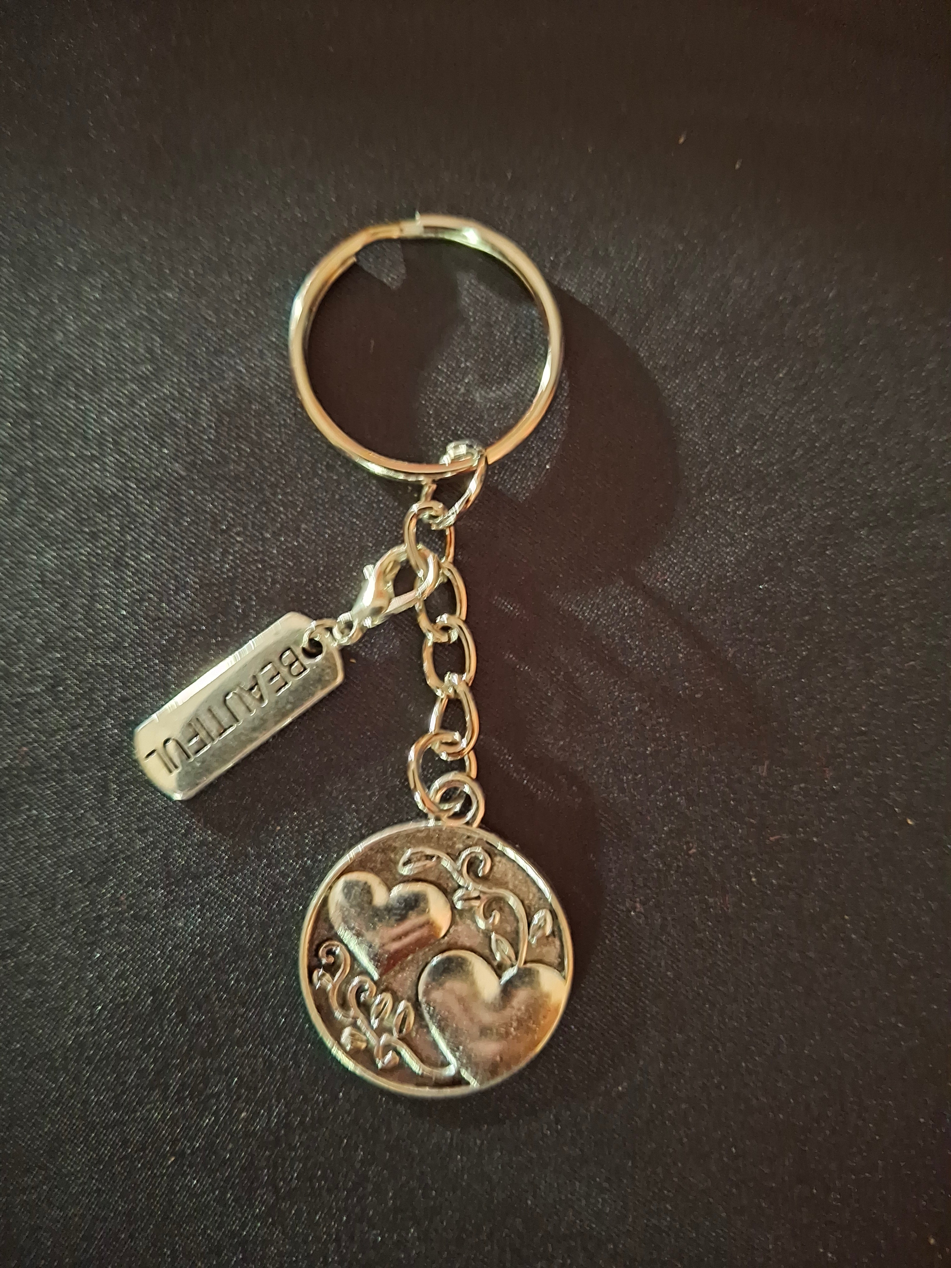 Bronze keychain with circular tag and rectangular pendant on a dark surface