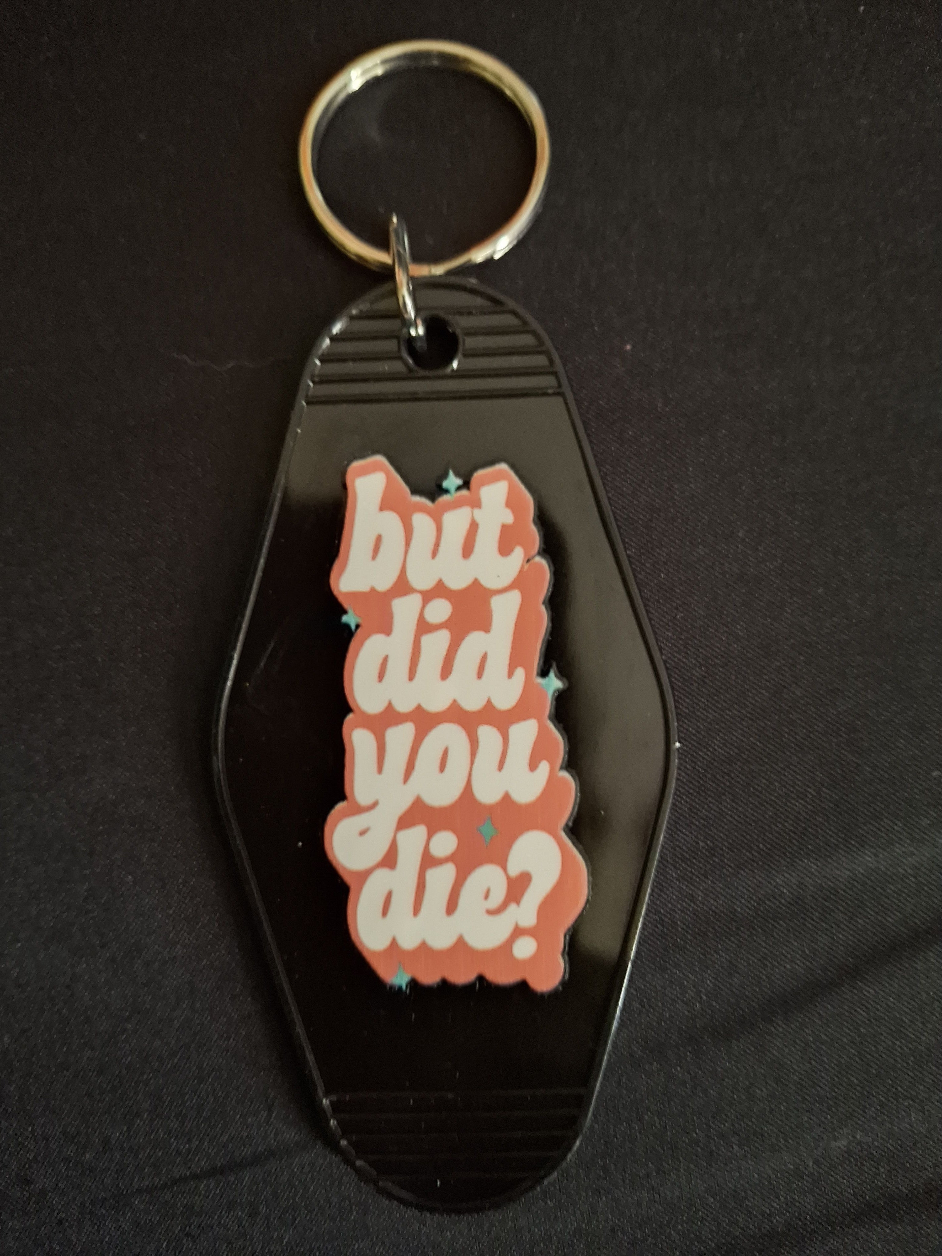 Black keychain with a pink and white graphic and text on a black background