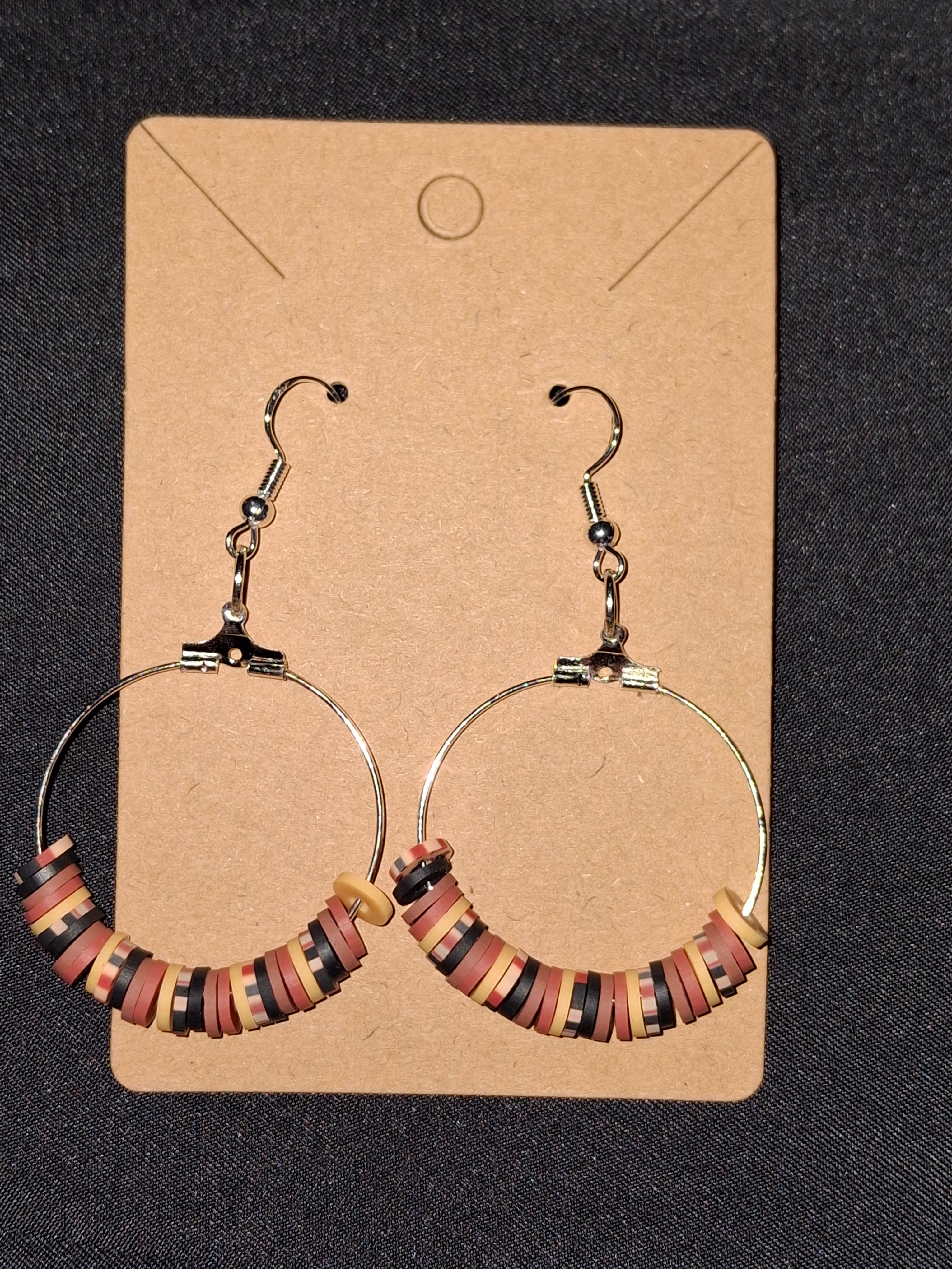 Pair of hoop earrings with colorful beads on a cardboard backing against a dark fabric background.
