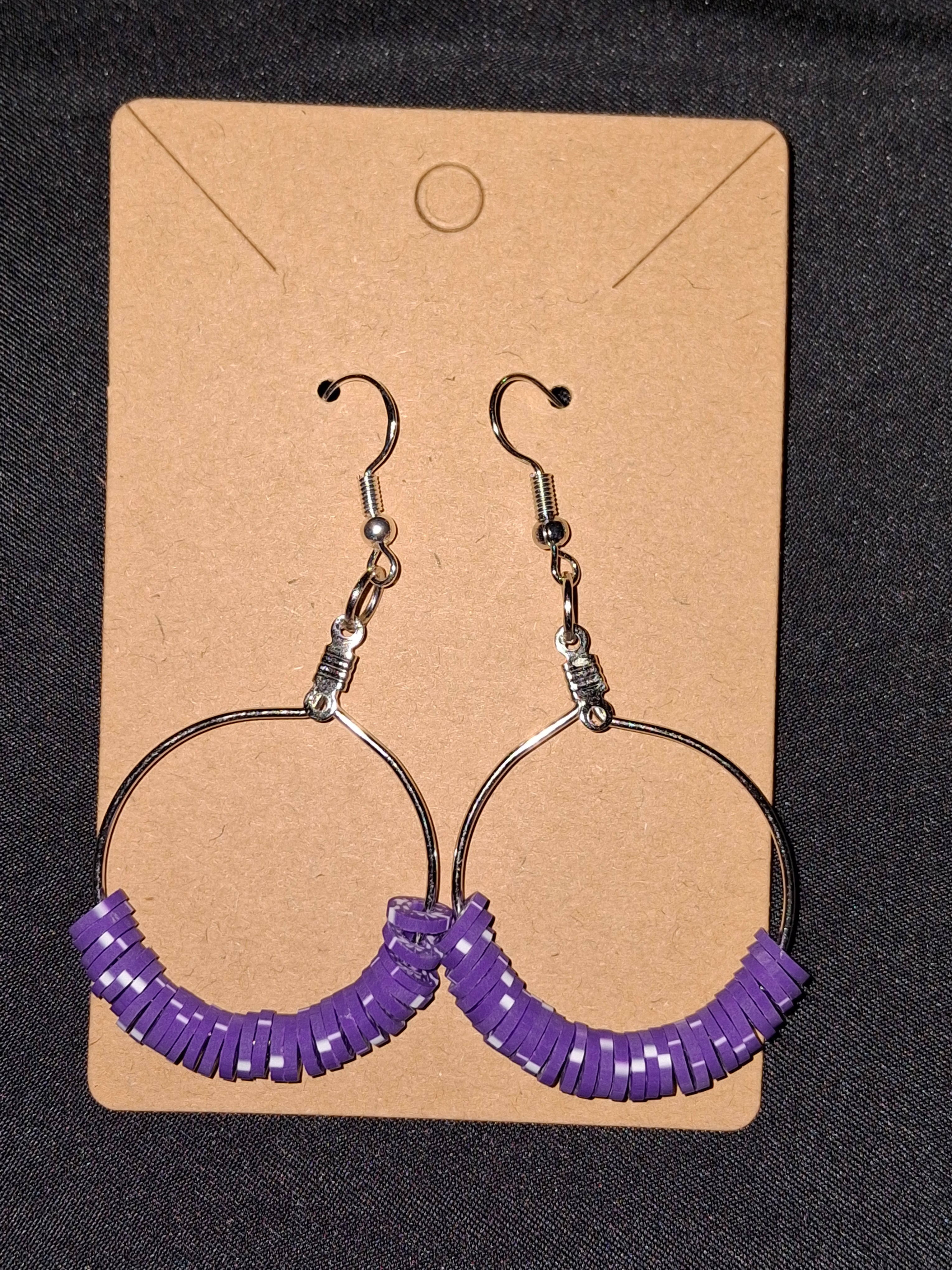 Pair of earrings with purple coils on a cardboard backing against a dark background