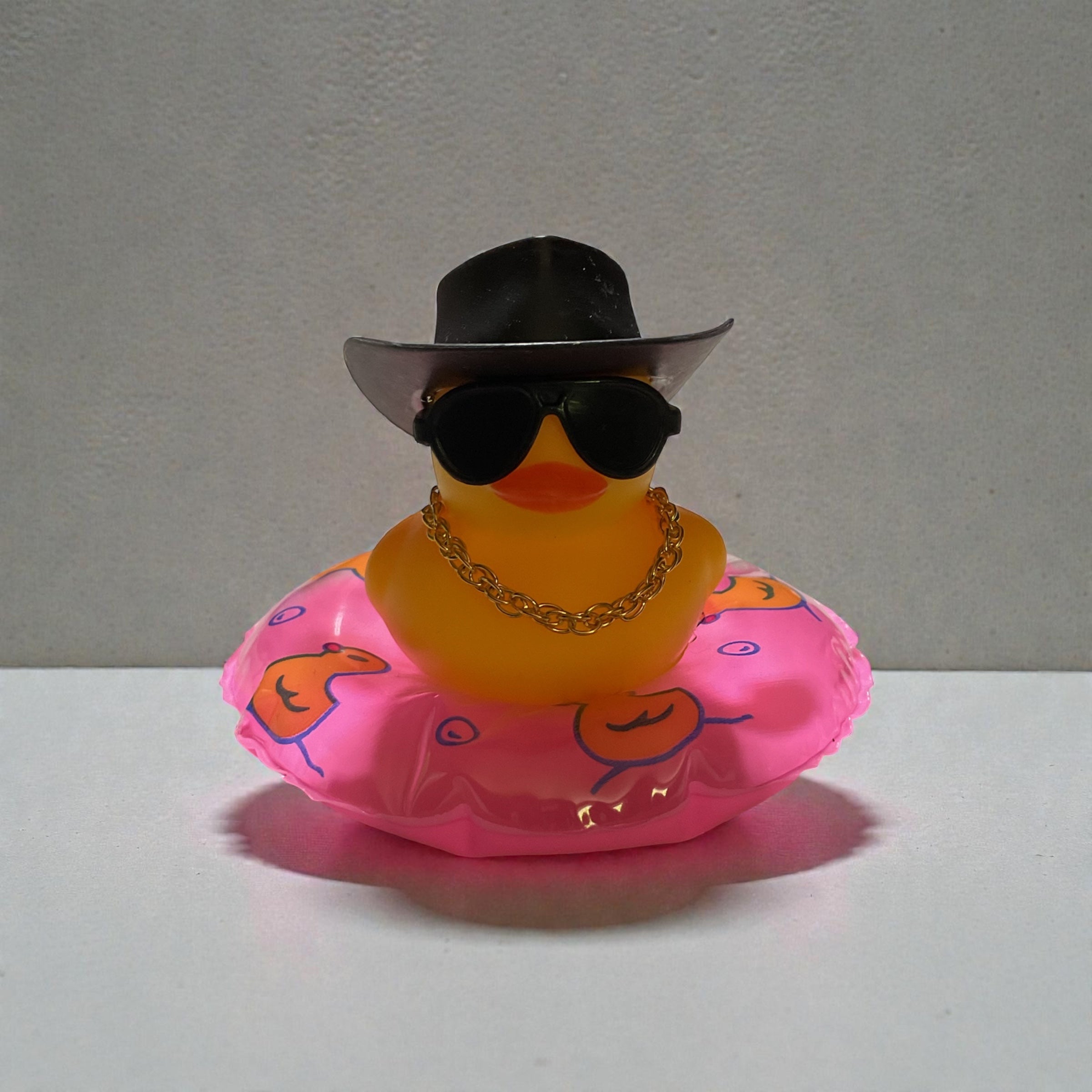 Yellow Duck with Black Cowboy Hat, Black Sunglasses, Gold Necklace sitting on a Pink Tube