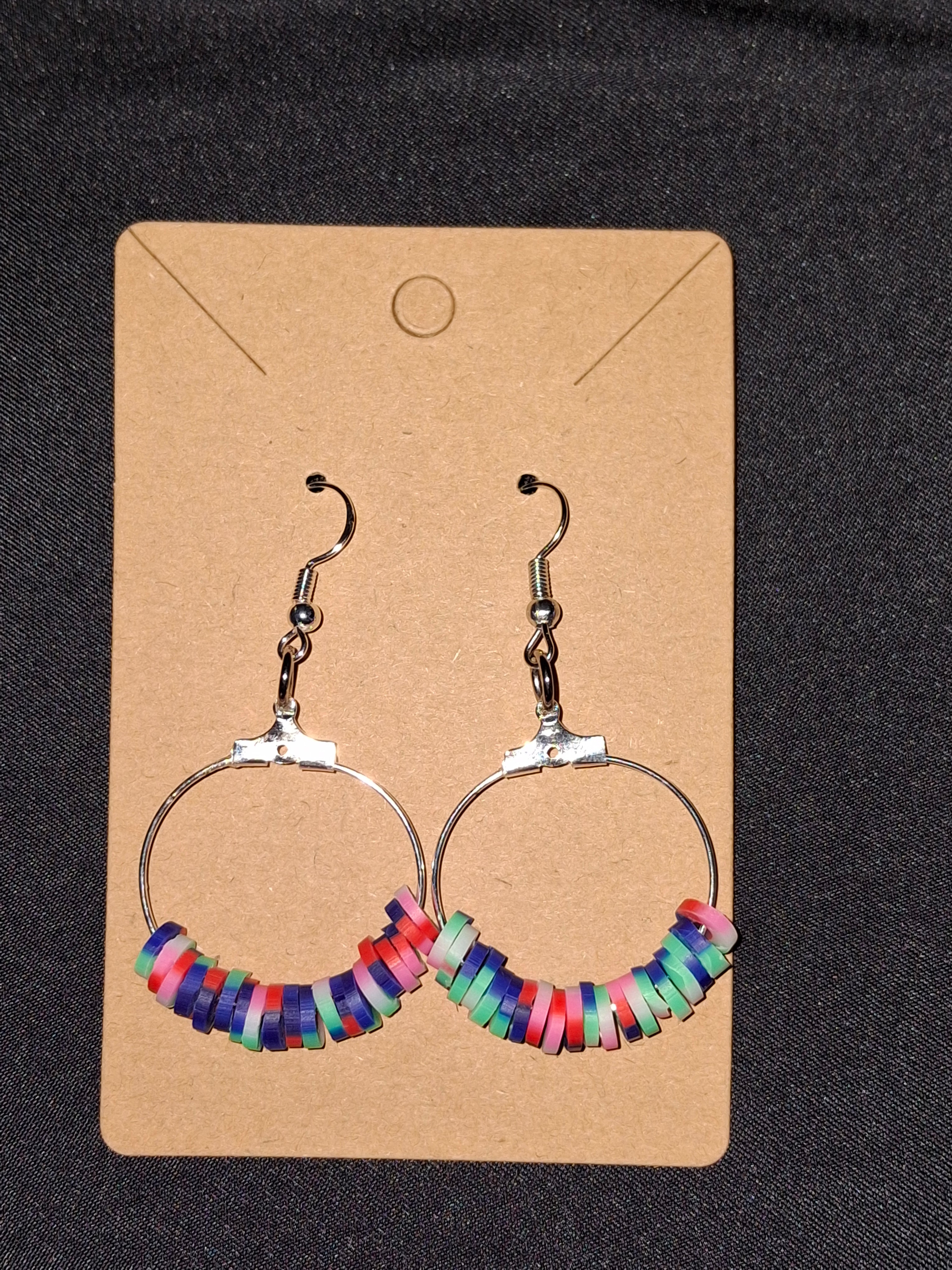 Colorful hoop earrings on a cardboard backing against a dark background