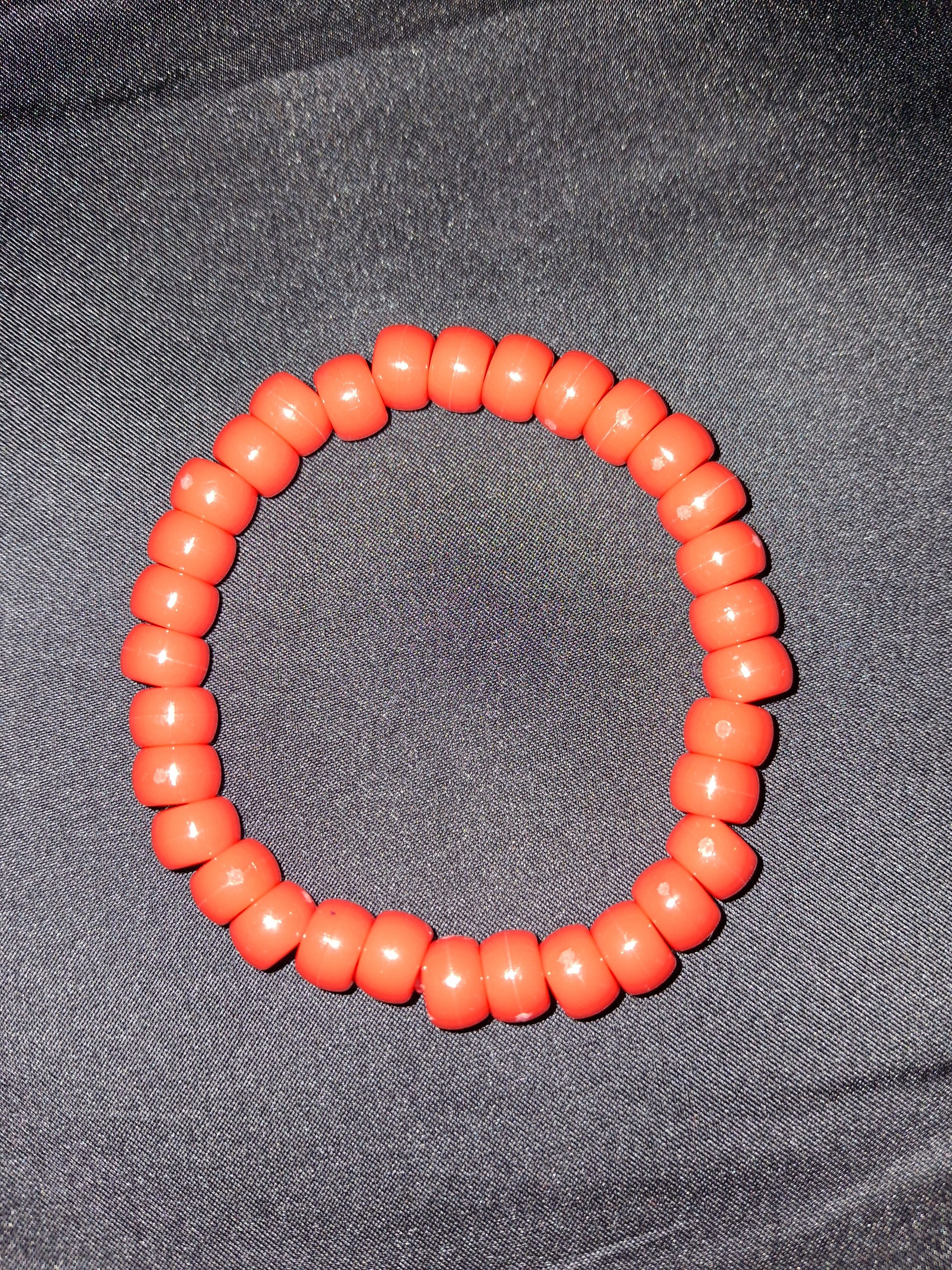 Neon orange beaded bracelet on a gray fabric background