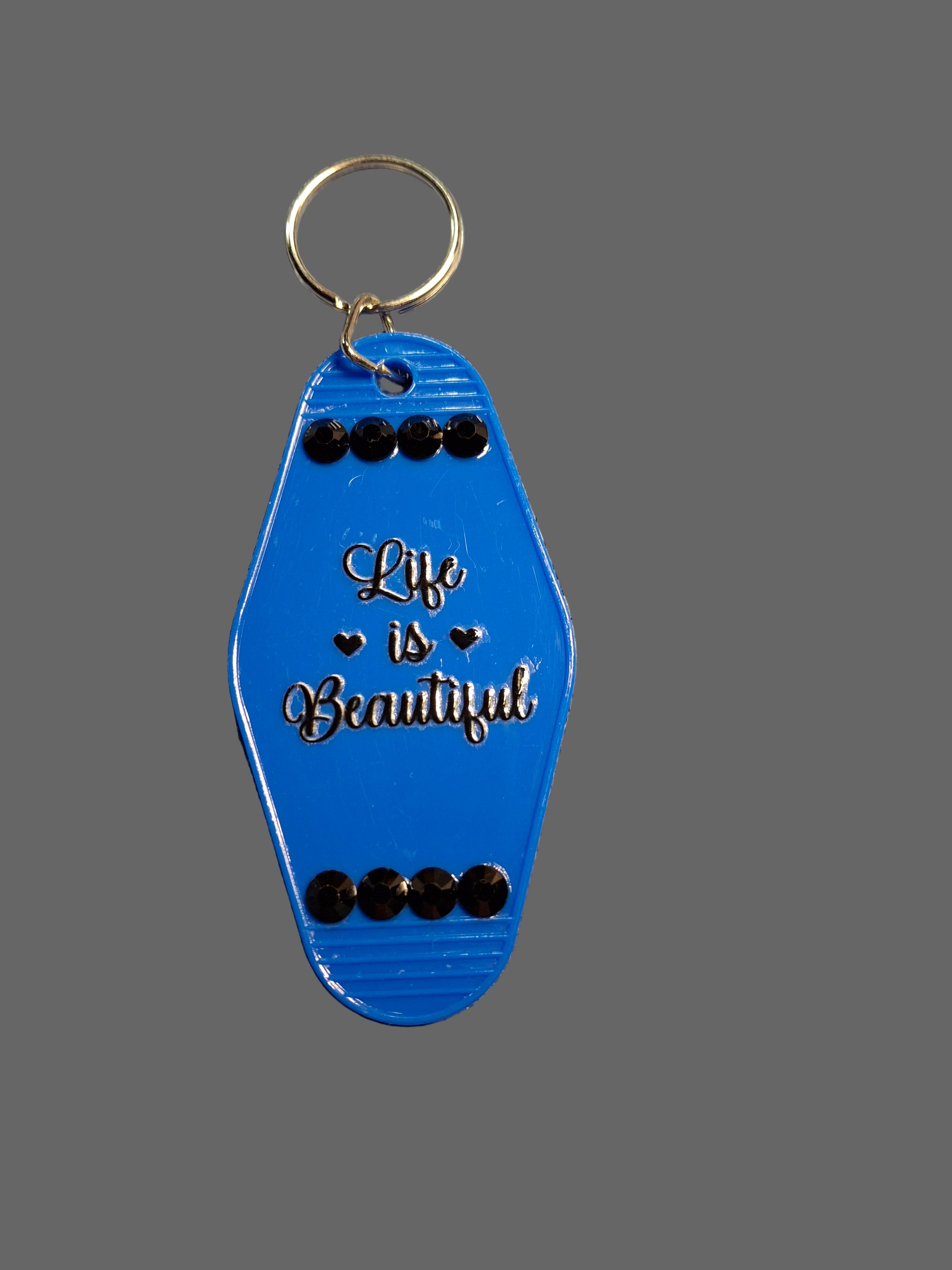 Blue keychain with 'Life is Beautiful' text on a textured gray surface