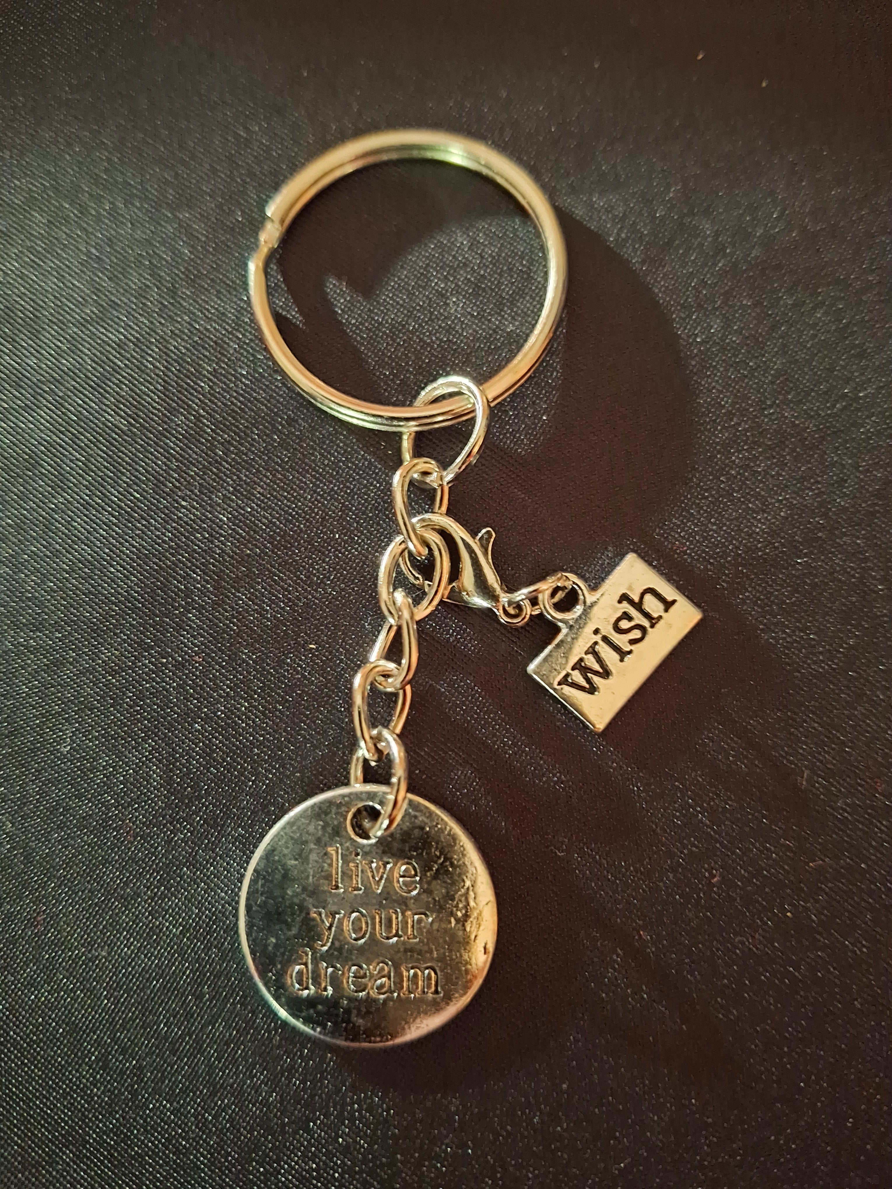 Gold keychain with a tag and circular pendant on a dark fabric background