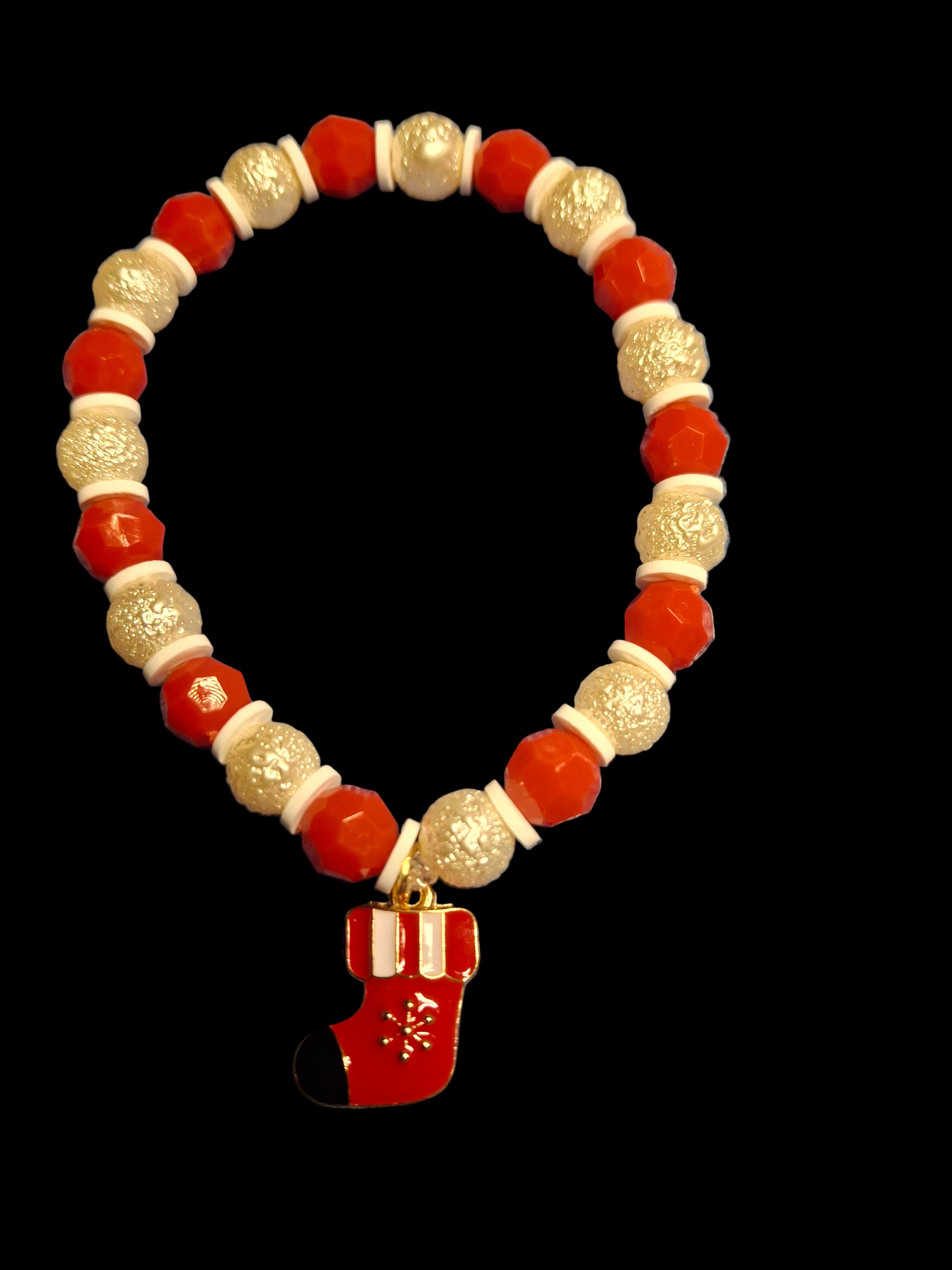 Bracelet with red, white, and gold beads and a red stocking charm on a black background