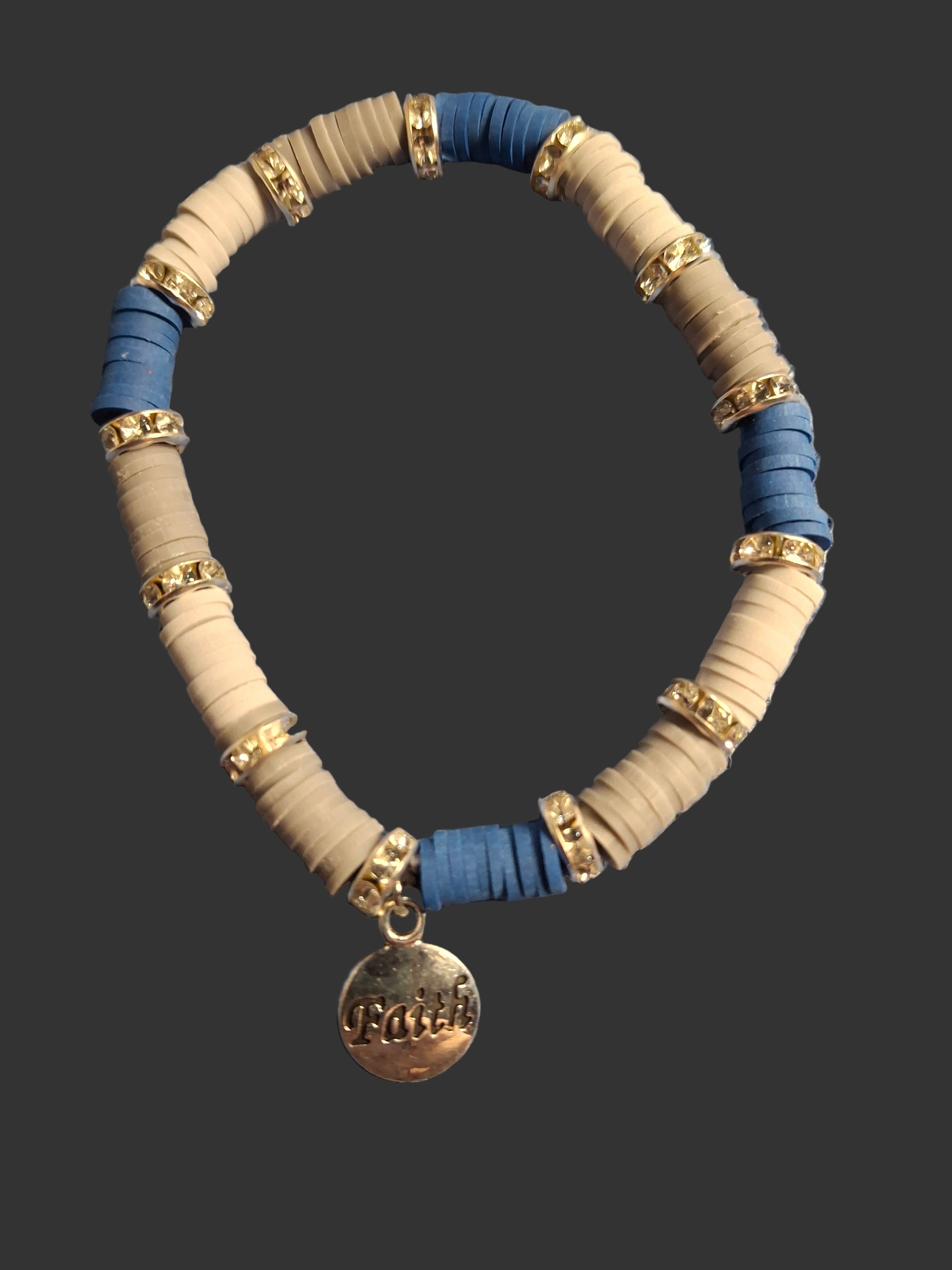 Bracelet with blue and beige beads and a gold 'Faith' charm on a dark background